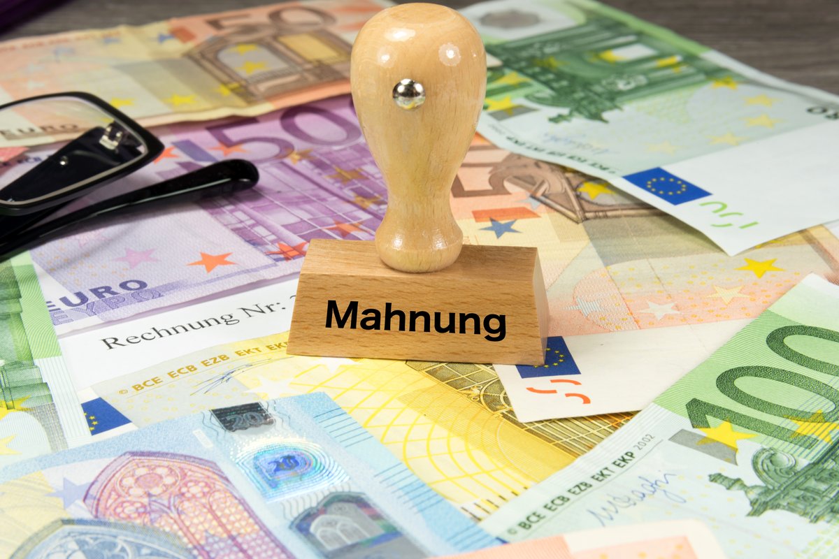 Holzstempel mit der Aufschrift Mahnung auf Euro-Banknoten und einer Rechnung